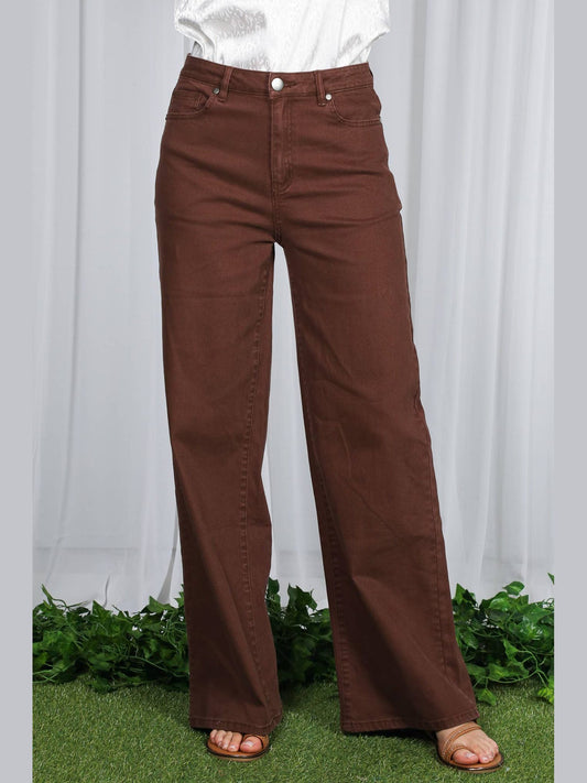 Brown pants worn by a person standing on grass with a white curtain background