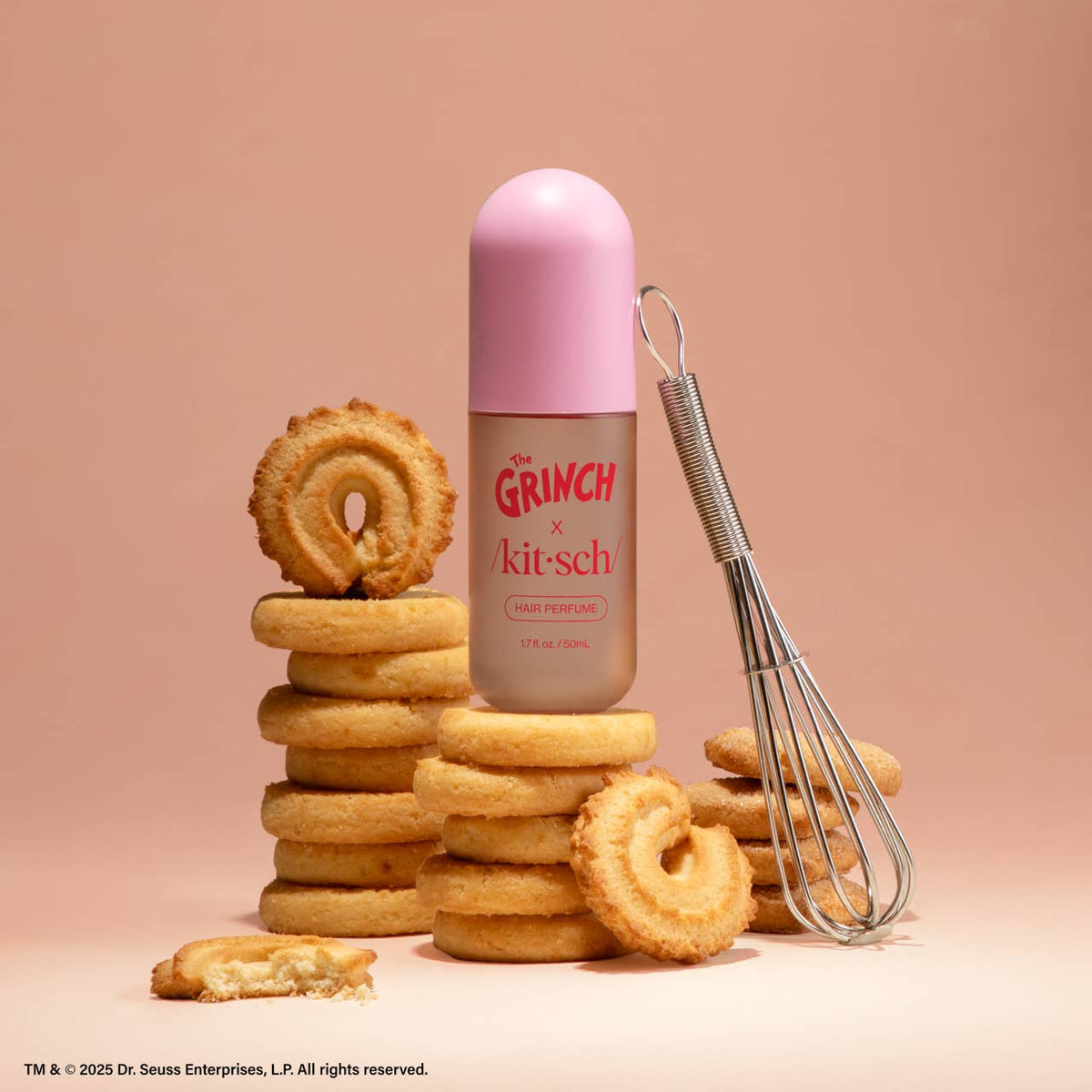 Pink bottle of 'The Grinch' x 'kitsch' hair perfume with cookies and a whisk on a beige background