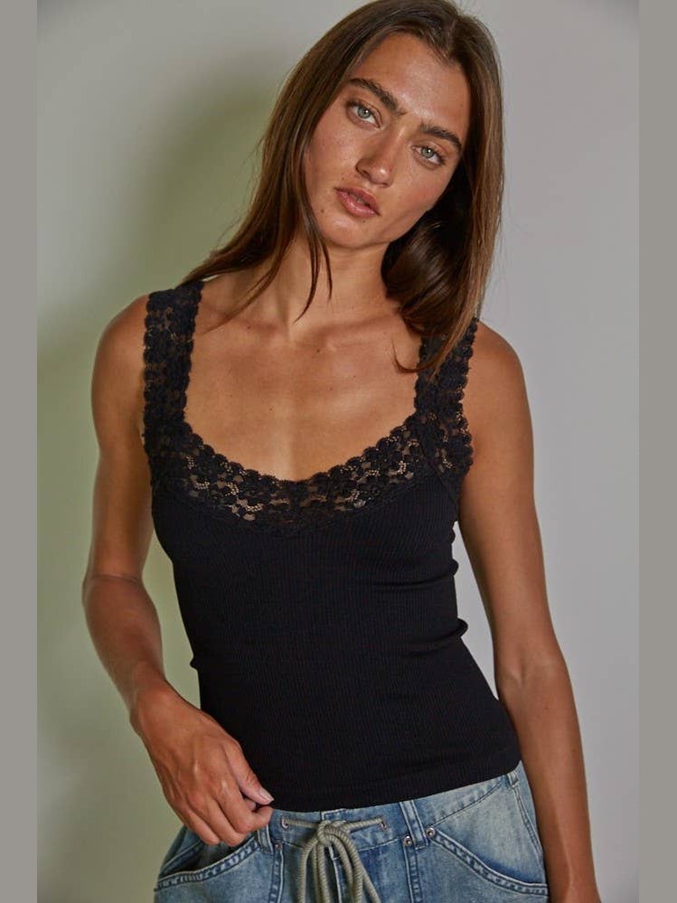 A woman wearing a black ribbed camisole top with a floral lace trim along the scoop neckline, paired with blue jeans, photographed against a neutral gray background.