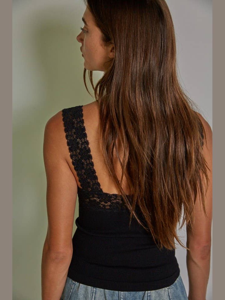 Woman wearing a black sleeveless top with lace detailing on the back, standing against a neutral background.