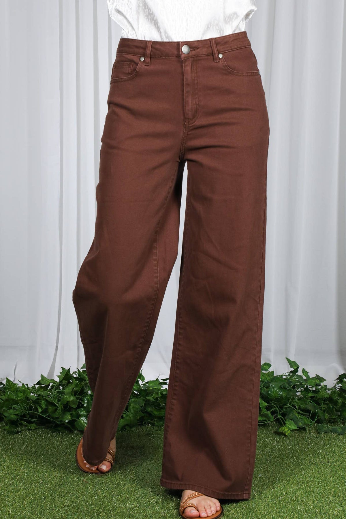 Brown pants worn by a person standing on grass with white curtains in the background